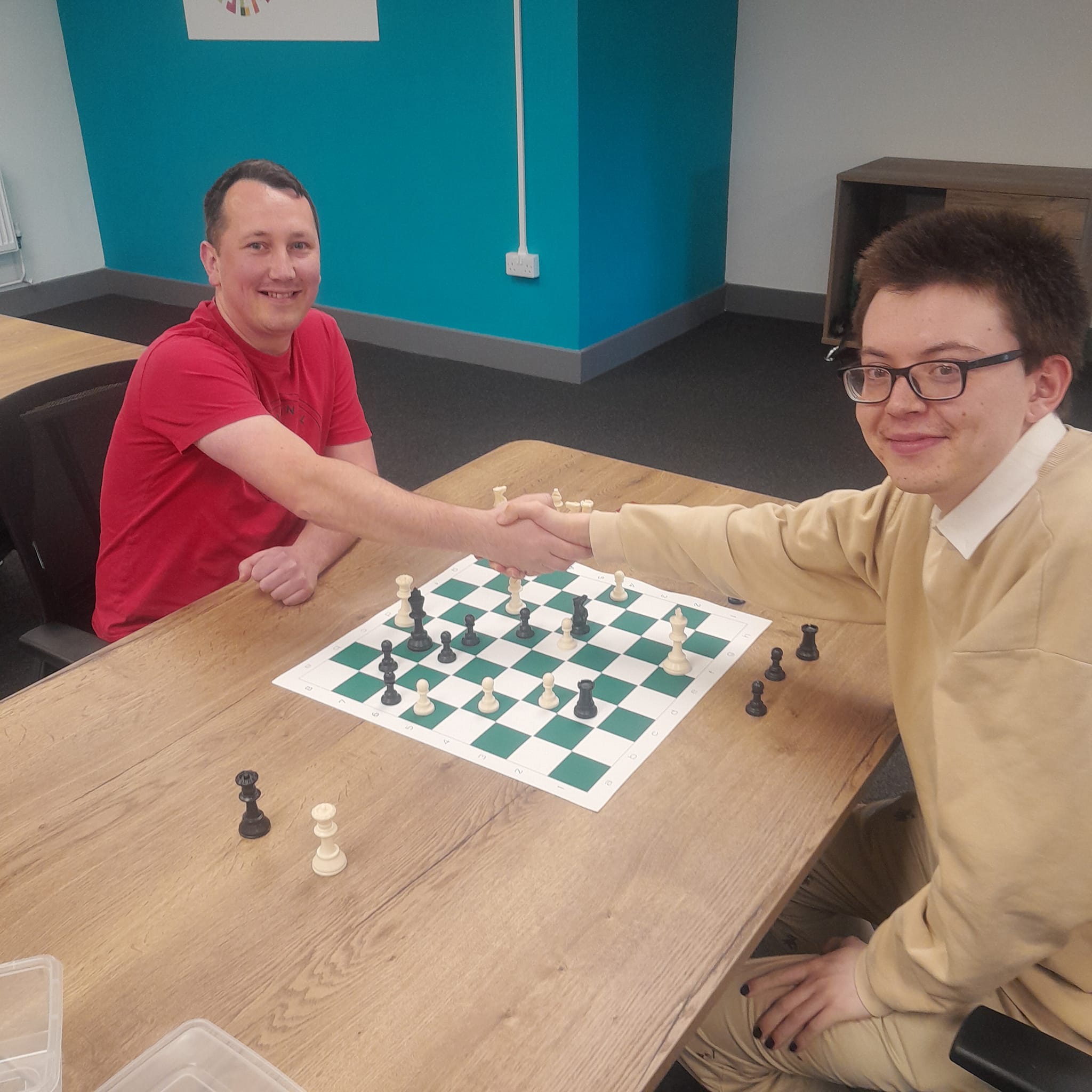 Two members shaking hands over a chessboard in the Manor Walks community room