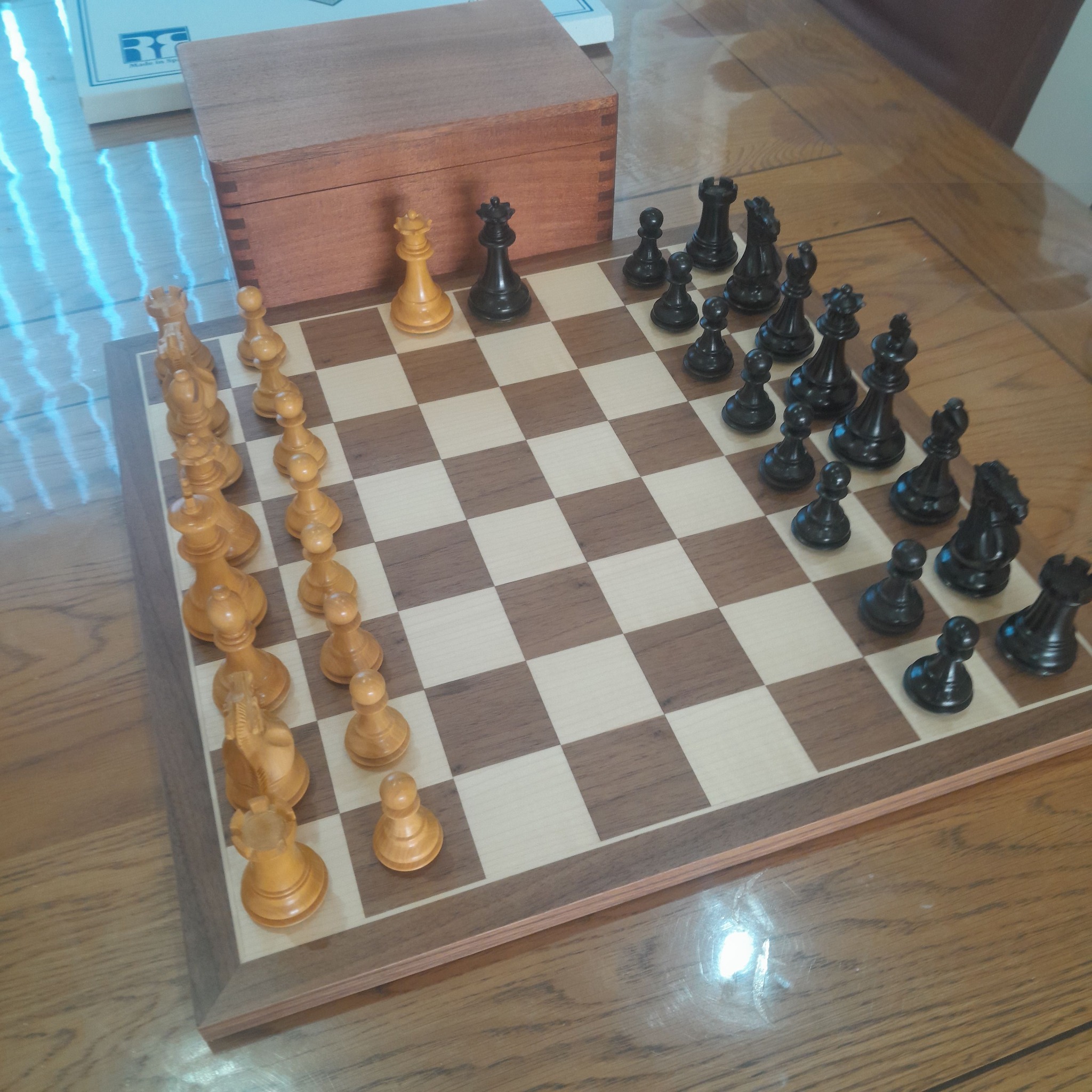 Wooden chess set with boxwood and ebonised pieces set up beside its wooden storage box