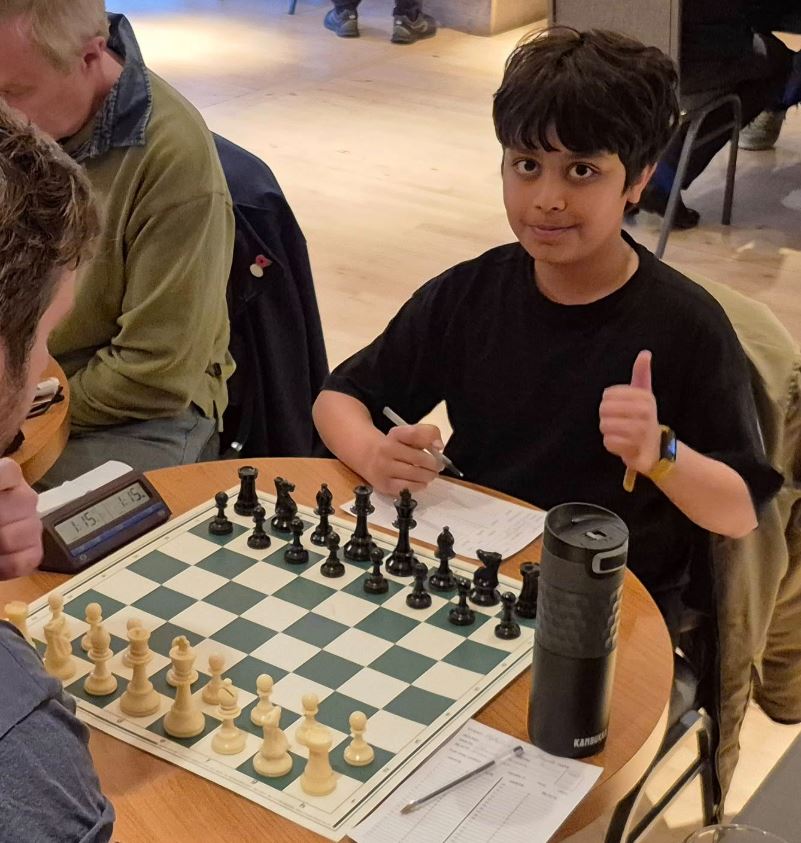 Young player giving a thumbs up behind the black pieces during a club game